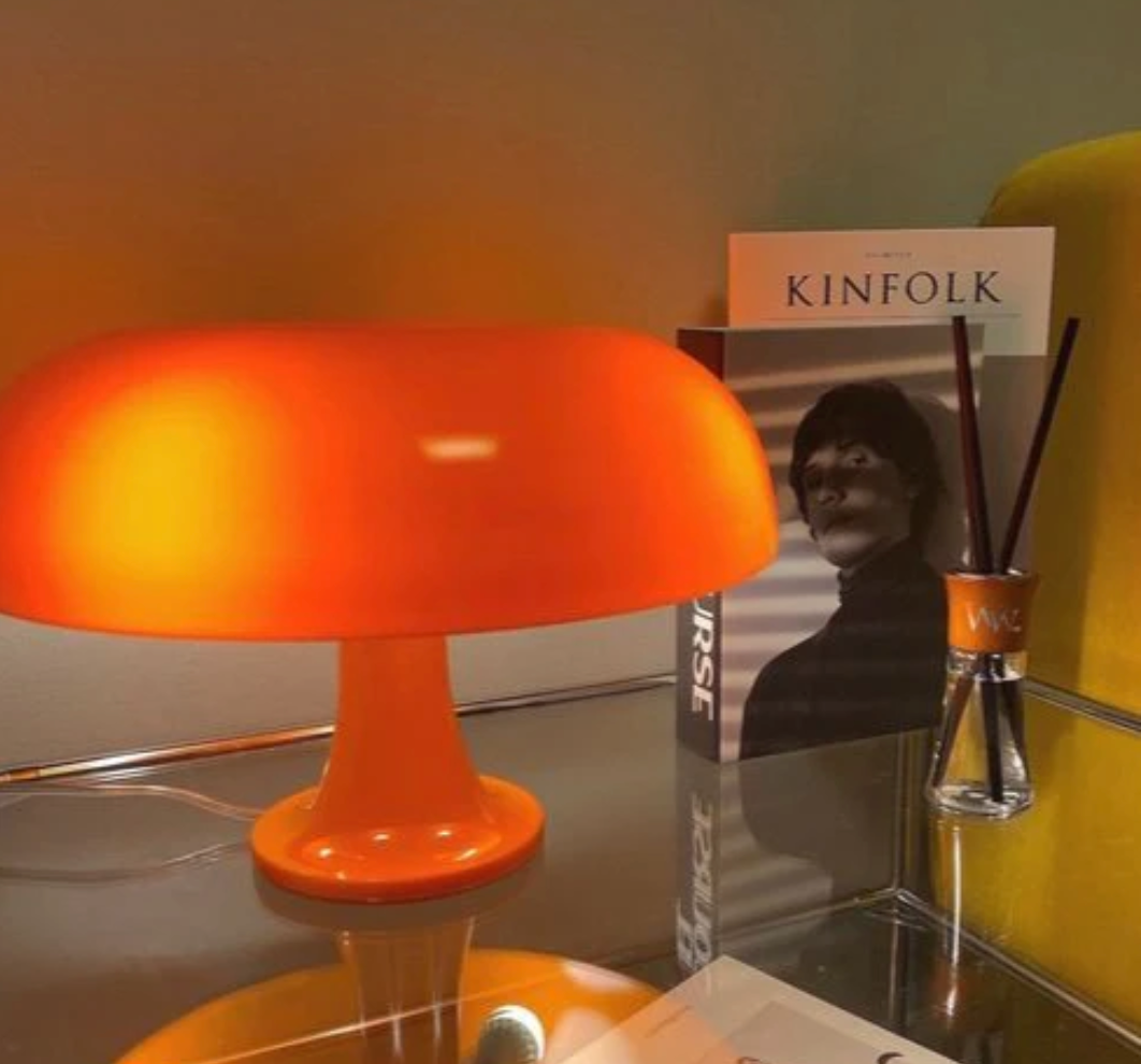Orange mushroom-shaped LED table lamp on a glass table with books and a diffuser.
