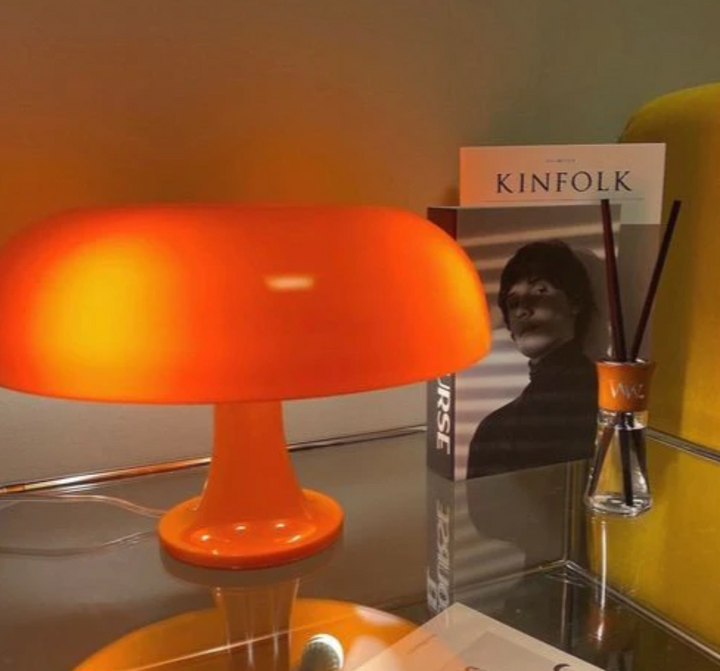 Orange mushroom-shaped LED table lamp on a glass table with books and a diffuser.