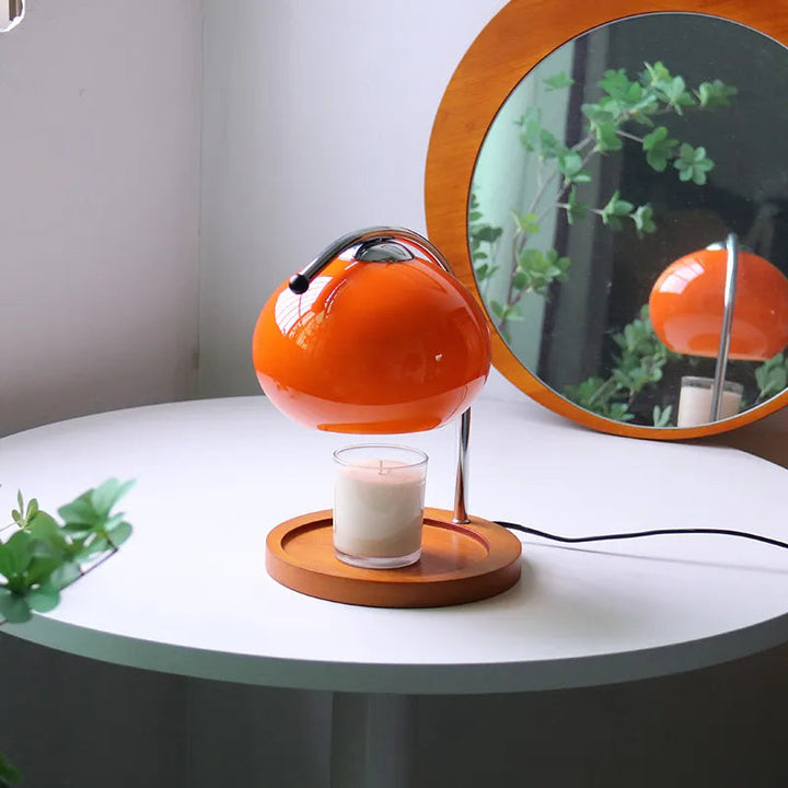 Orange glass candle warmer lamp with a wooden base and a candle underneath, reflected in a mirror.