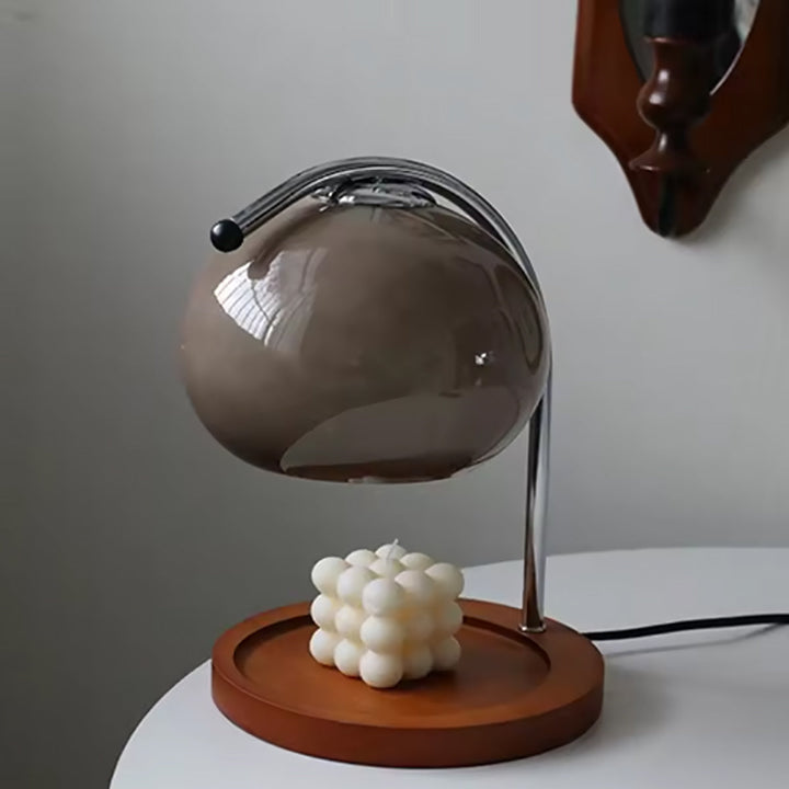 Metal and glass candle warmer lamp with a brown globe shade over a white cube candle on a wooden base.