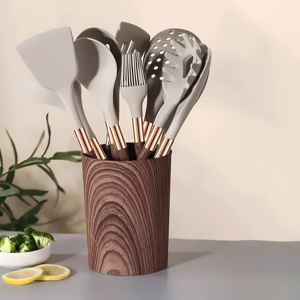 A set of 10 grey silicone kitchen utensils with rose gold handles in a wooden holder.
