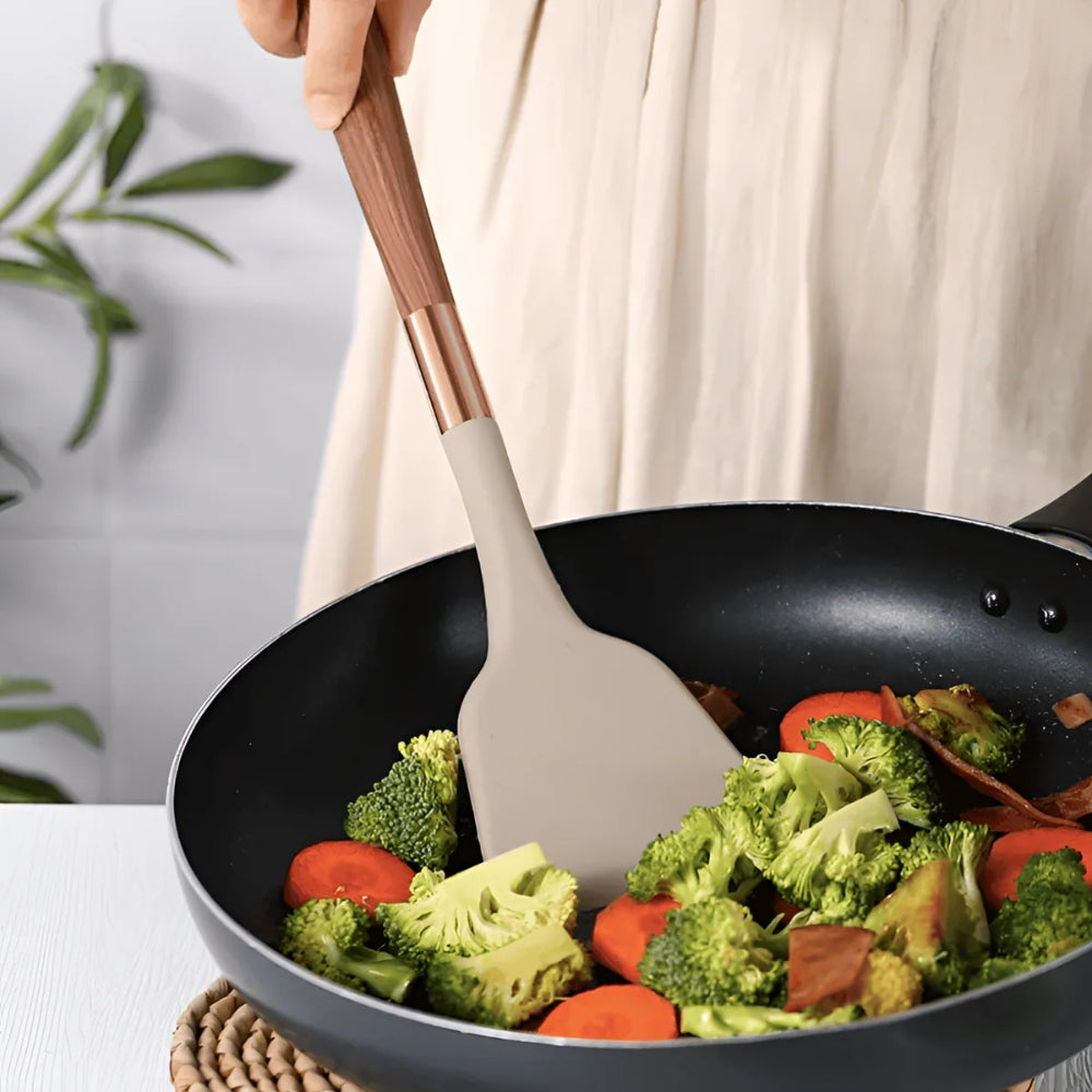A beige silicone spatula with a wooden handle stirs broccoli and carrots in a black wok.