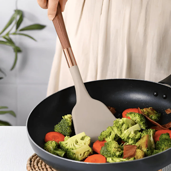 A beige silicone spatula with a wooden handle stirs broccoli and carrots in a black wok.