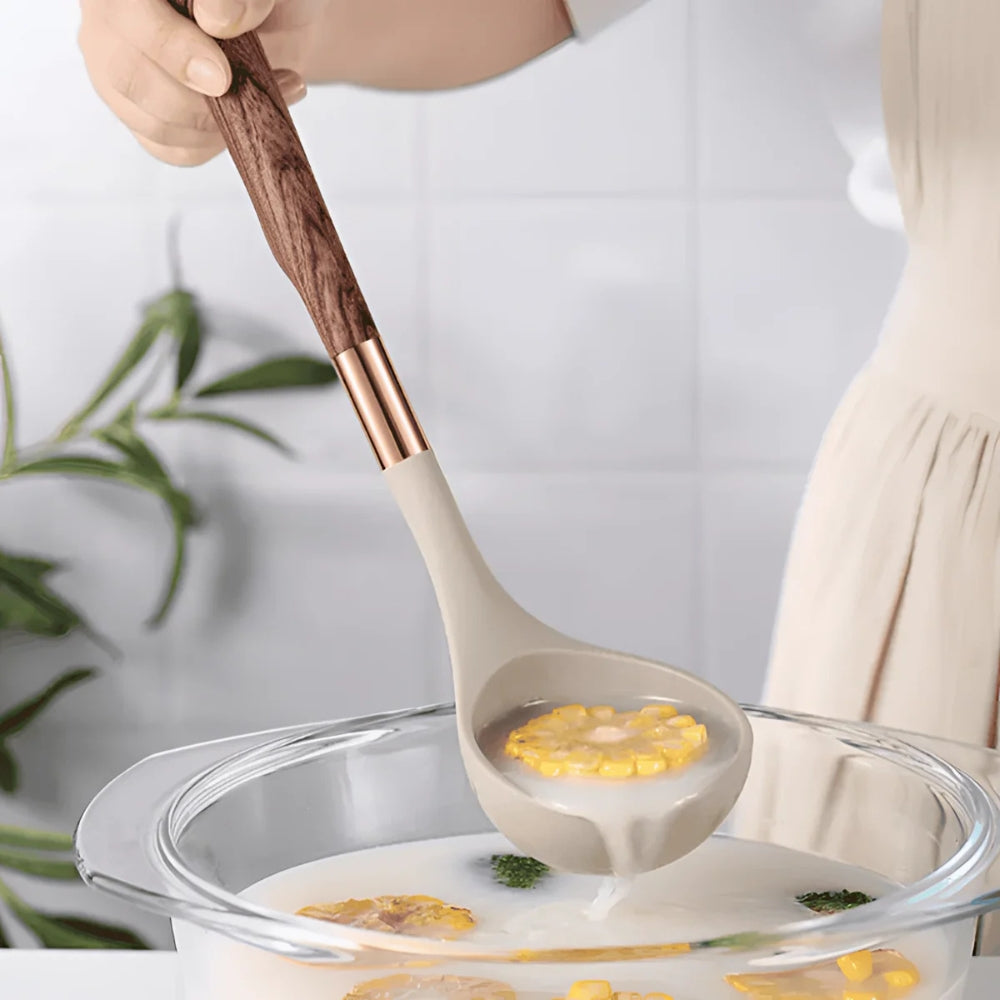 A silicone ladle with a wood-grain handle scoops soup from a glass bowl.