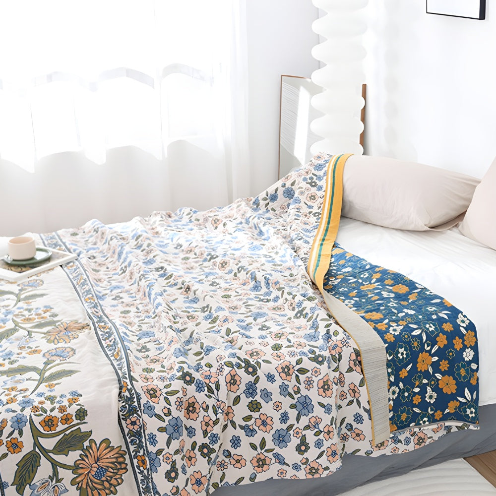 A boho floral blanket with a blue floral pattern on one side and a white floral pattern on the other, draped on a bed.