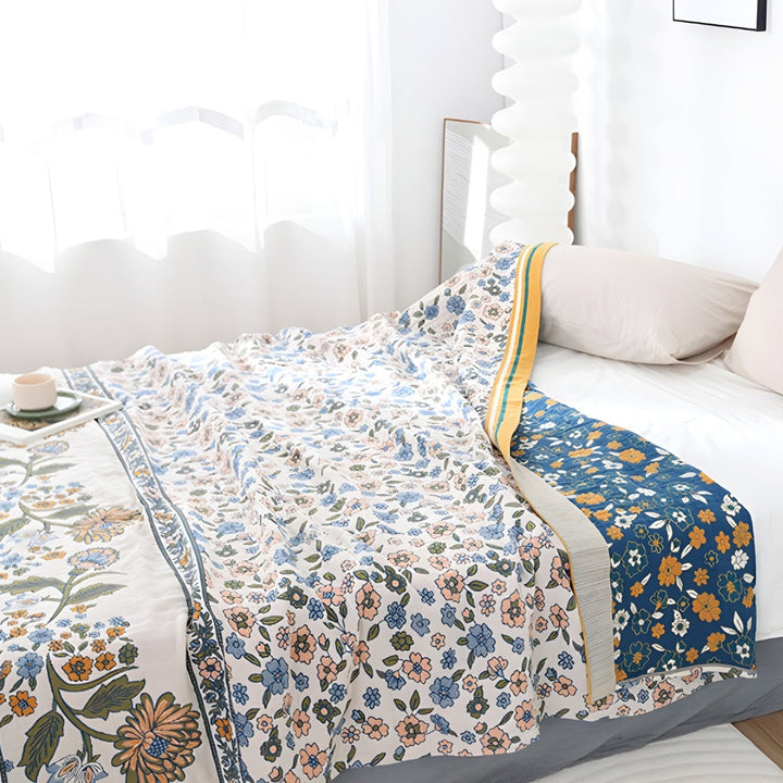 A boho floral blanket with a blue floral pattern on one side and a white floral pattern on the other, draped on a bed.