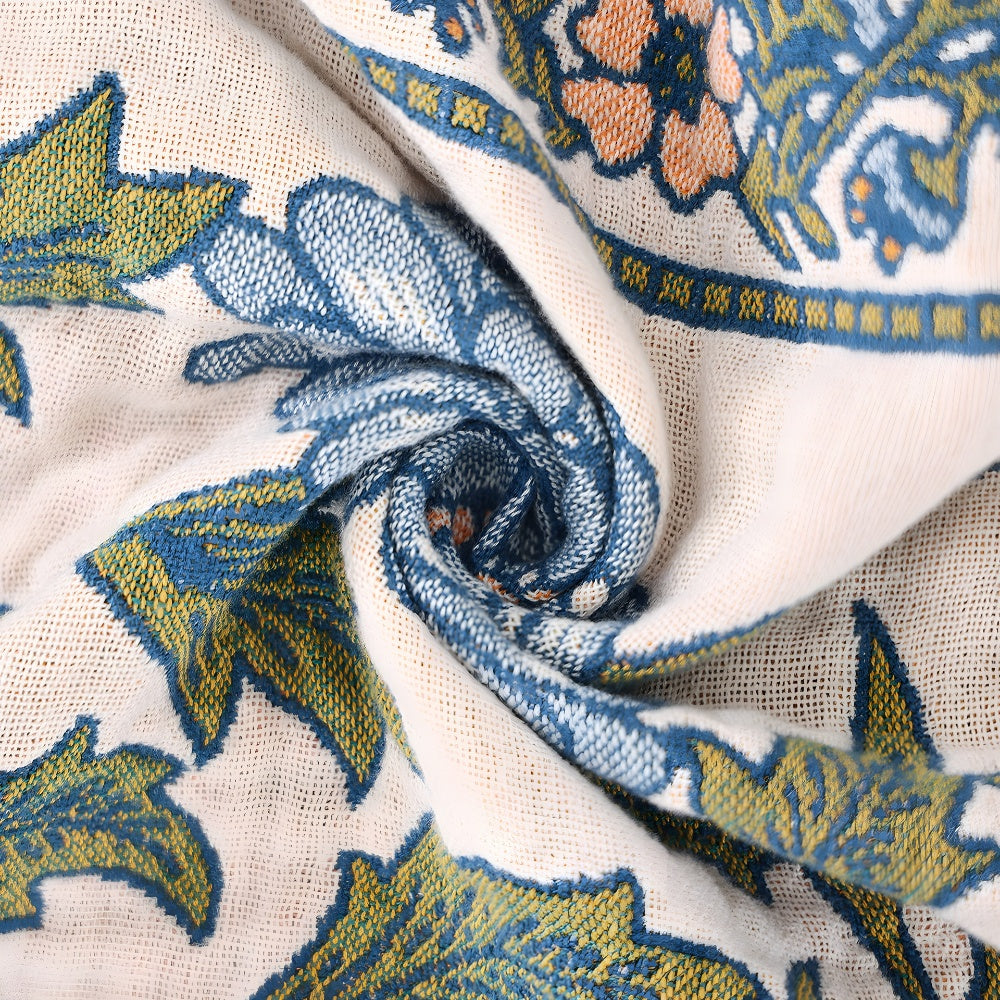 Close-up of a cream-colored cotton blanket with a boho floral pattern in blue, green, and orange.