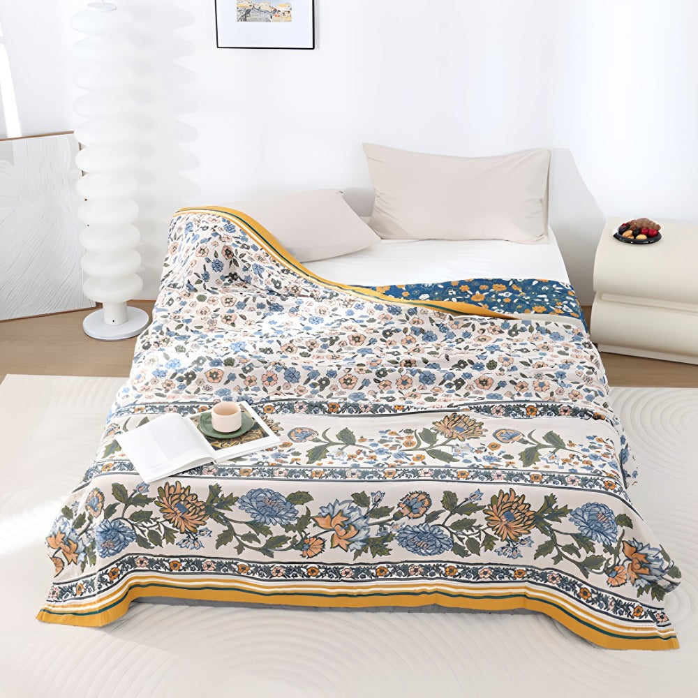 Meadow Bliss Boho Floral Blanket draped on a bed with pillows and a book.