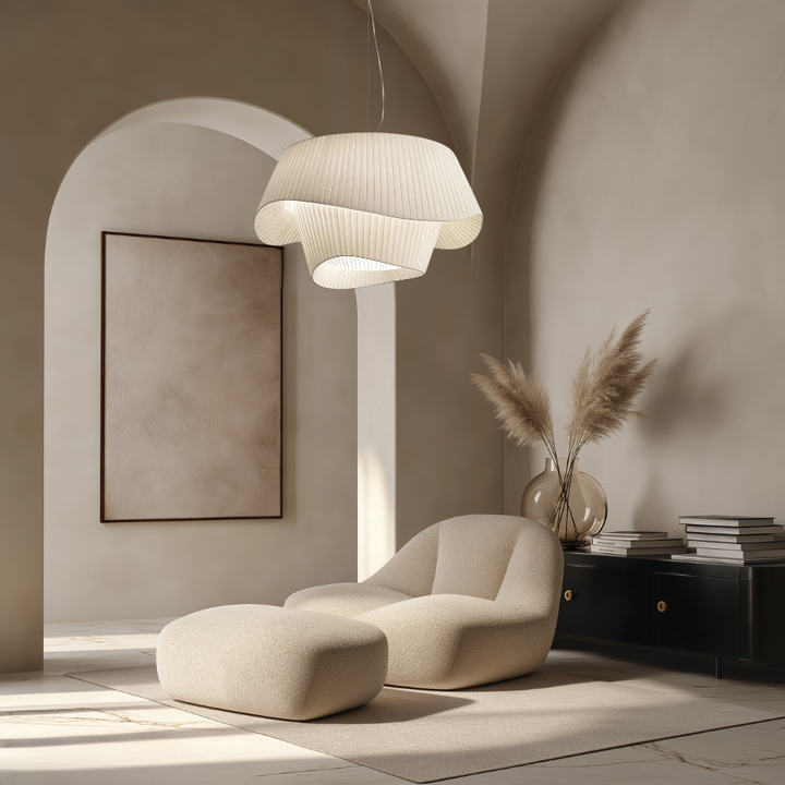 A modern, layered pendant light with a pleated texture hangs above a cream armchair and ottoman.