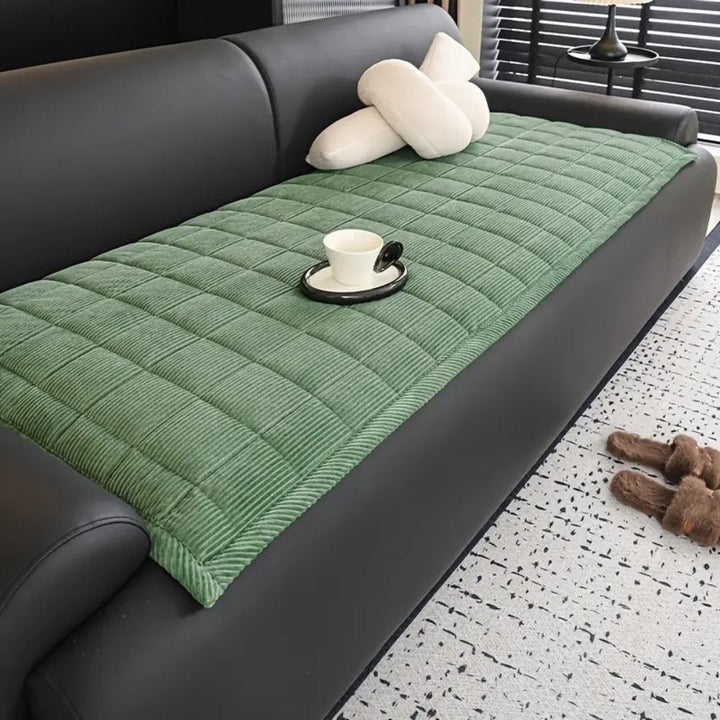 Green quilted microfiber couch cover mat with a white cup and saucer on it.