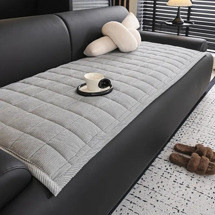 Gray quilted microfiber couch cover mat with a cup and saucer on it.