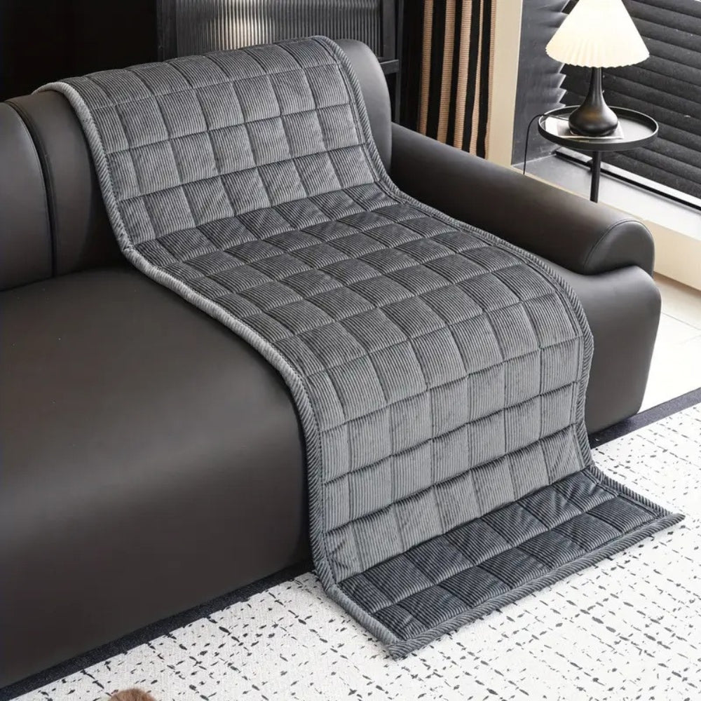 Gray quilted microfiber couch cover mat draped over a dark leather sofa.