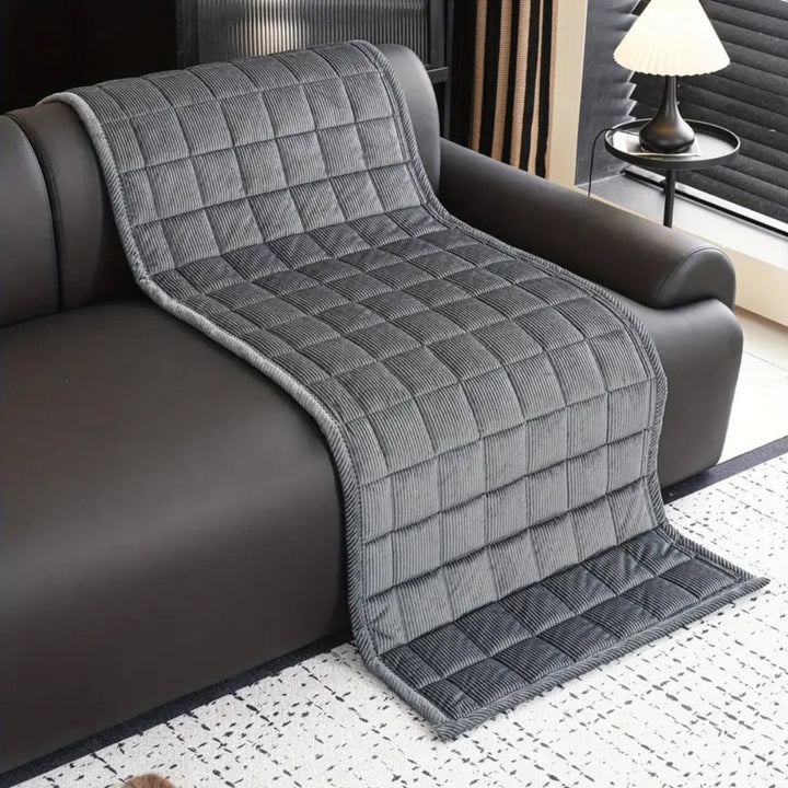Gray quilted microfiber couch cover mat draped over a dark leather sofa.