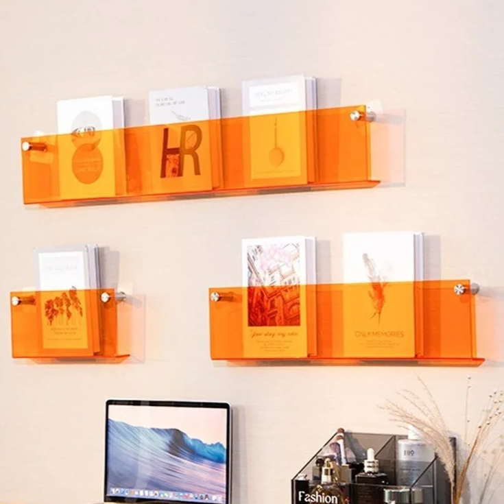 Orange acrylic floating shelves mounted on a wall displaying books and magazines.