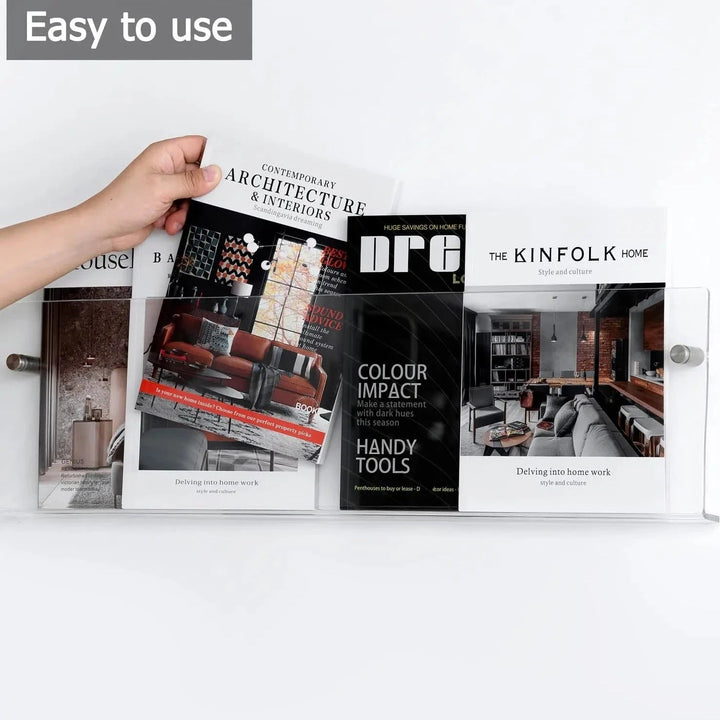 Clear acrylic floating shelf holding several magazines and books against a white wall.