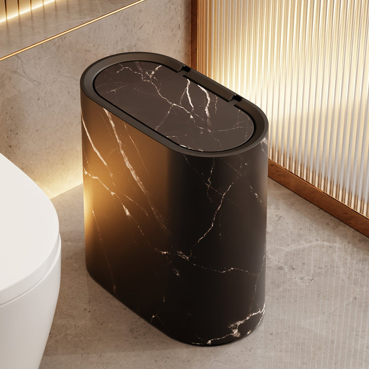 Black marble trash can with an oval lid and a modern design, placed next to a white toilet.