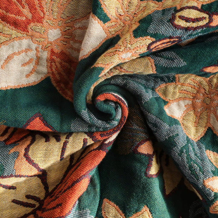Close-up of a green throw blanket with a swirling floral pattern in orange, yellow, and cream.