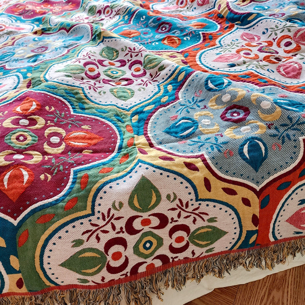 A close-up of a cotton blanket with a colorful Moroccan mosaic pattern and fringed edges.