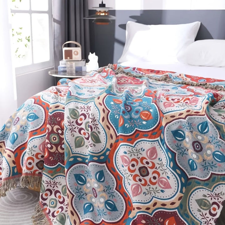A colorful Moroccan mosaic patterned cotton blanket with tassels draped over a bed.