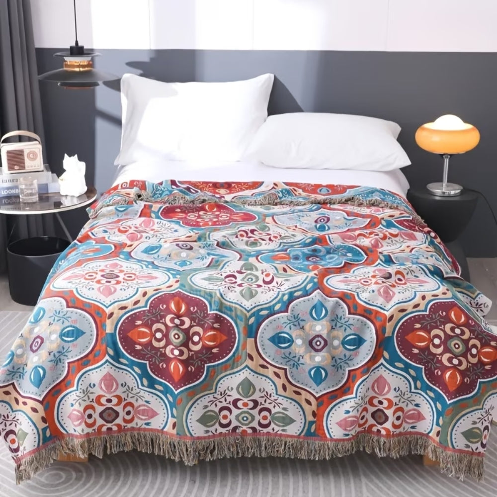 A cotton blanket with a colorful Moroccan mosaic pattern and fringed edges draped over a bed.