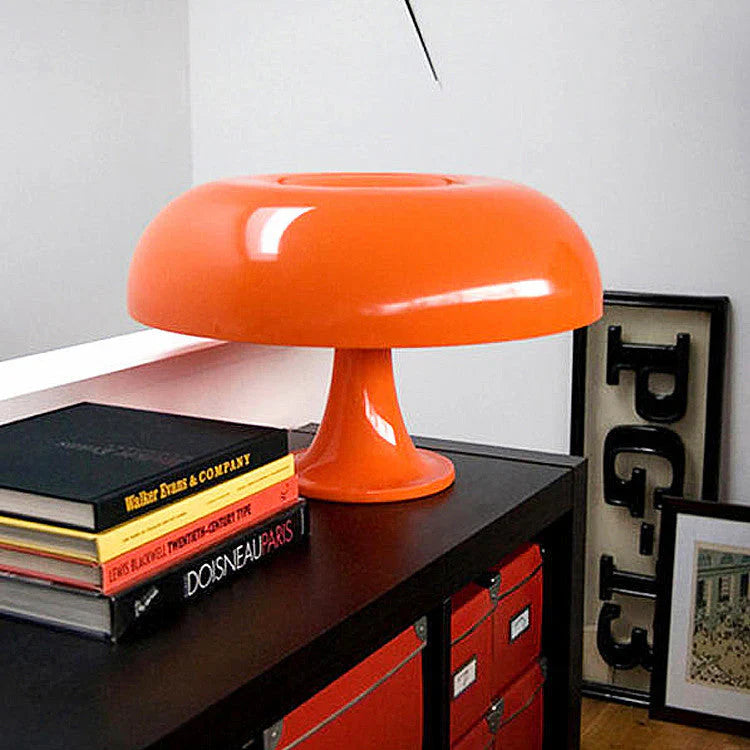 Orange mushroom-shaped LED table lamp on a black shelf with books.