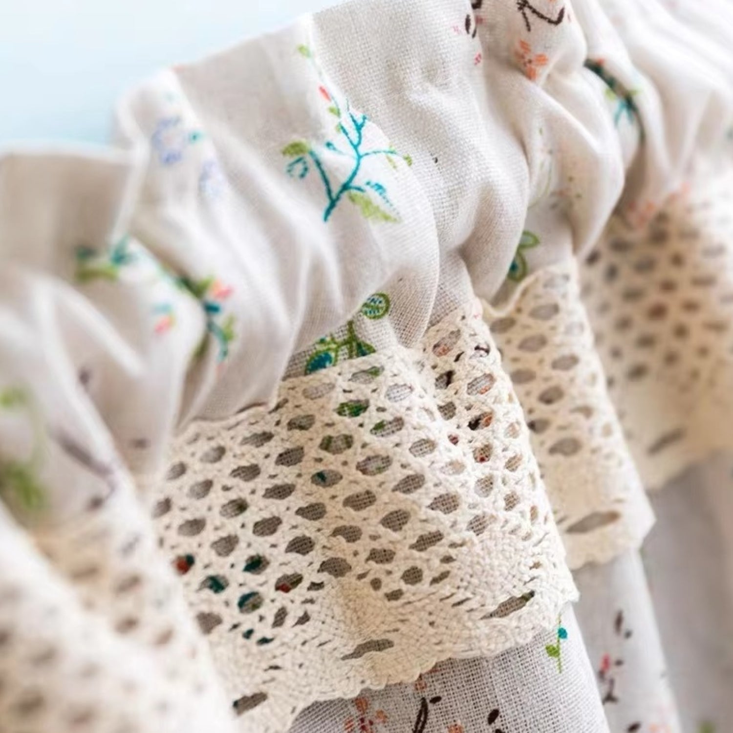 Close-up of a white kitchen curtain with a floral pattern and lace trim.