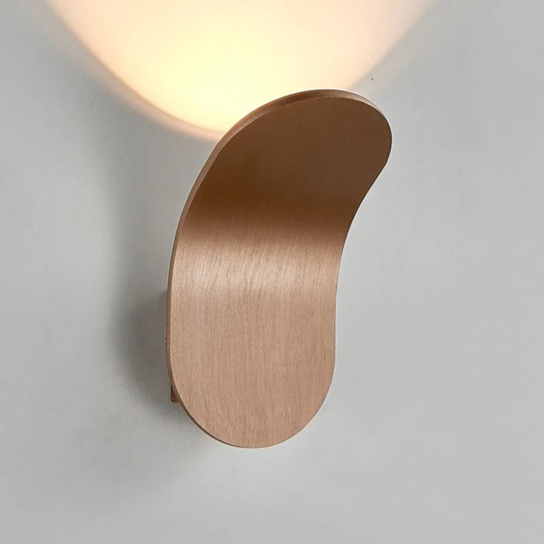 Minimalist LED wall sconce with a curved, wood-like finish, casting a warm light upwards.