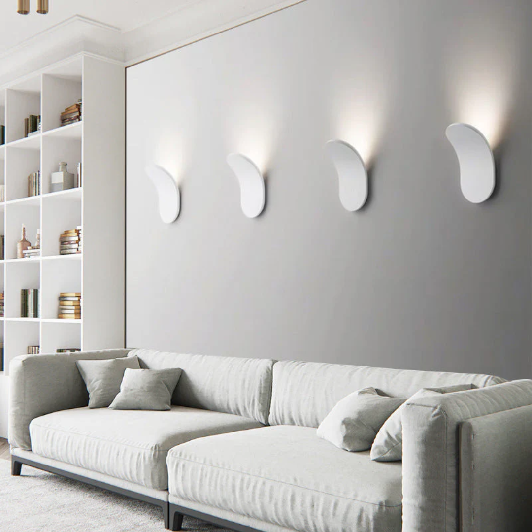 Four white minimalist LED wall sconces mounted on a grey wall above a light grey sectional sofa.