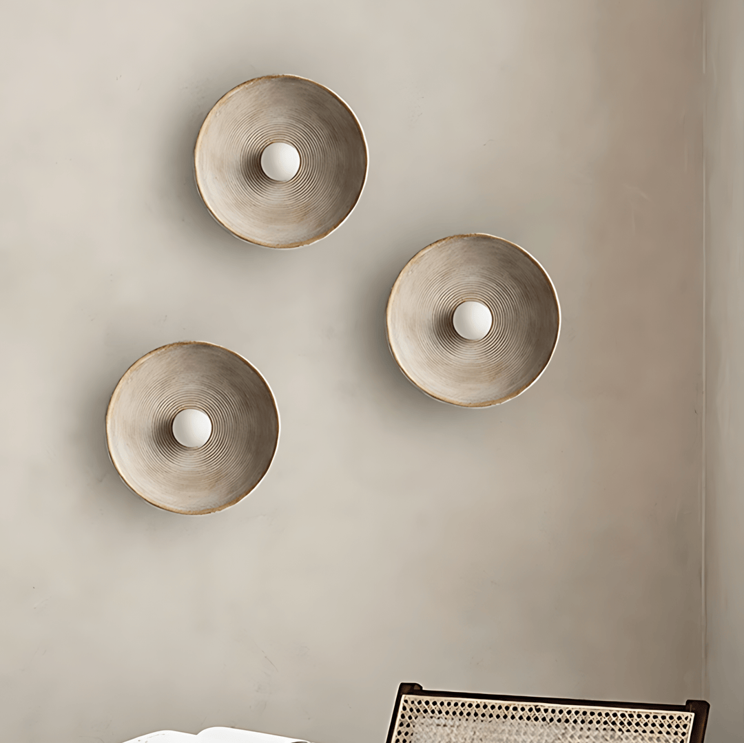 Three textured wall sconces with a central white bulb against a neutral wall.
