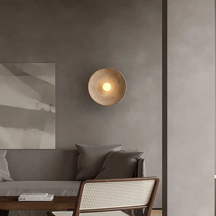 Textured wall sconce with a warm light, mounted on a grey wall above a sofa.