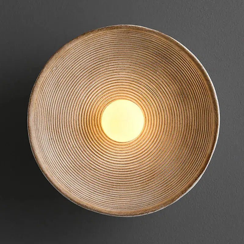 Textured wall sconce with concentric ridges and a warm yellow light in the center.