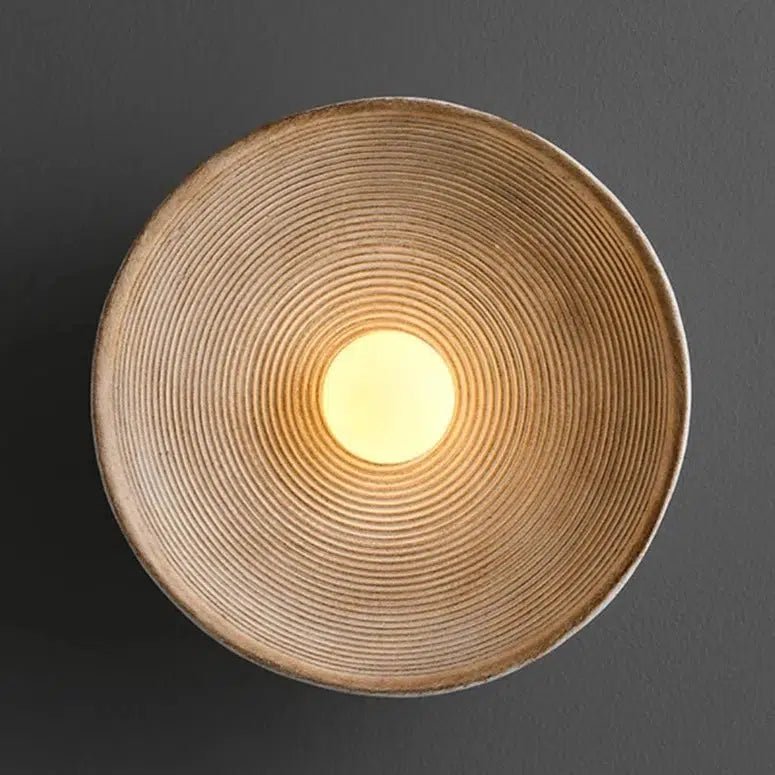 Textured wall sconce with concentric ridges and a warm light in the center.