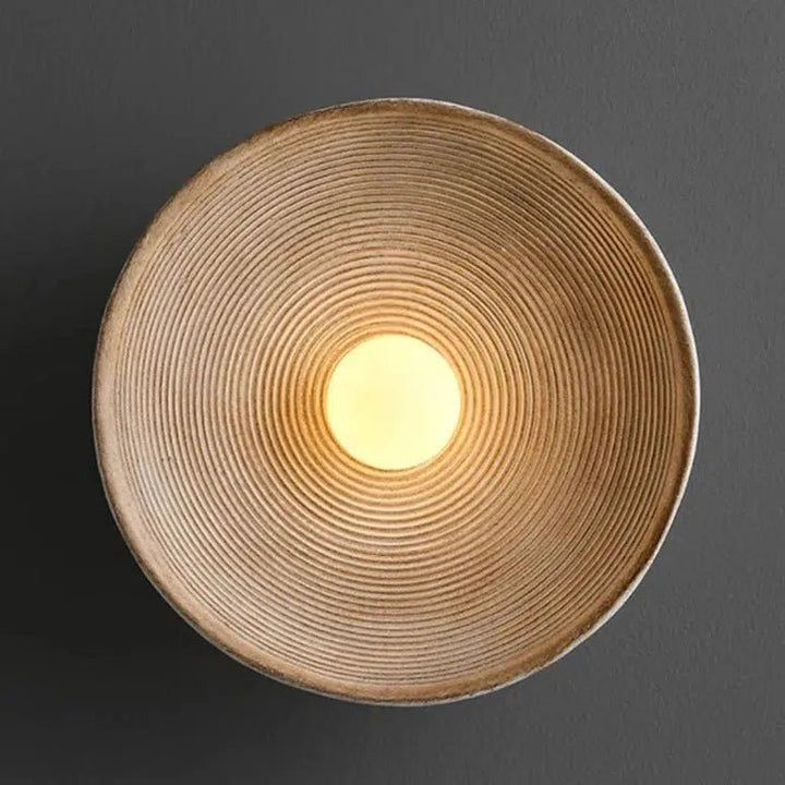Textured wall sconce with concentric ridges and a warm light in the center.