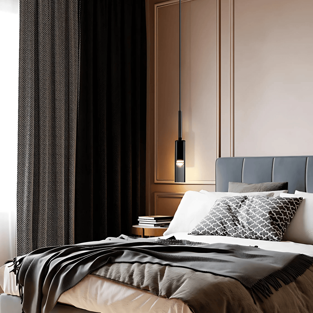 Black glass pendant light hanging over a bed with a grey headboard and patterned pillows.