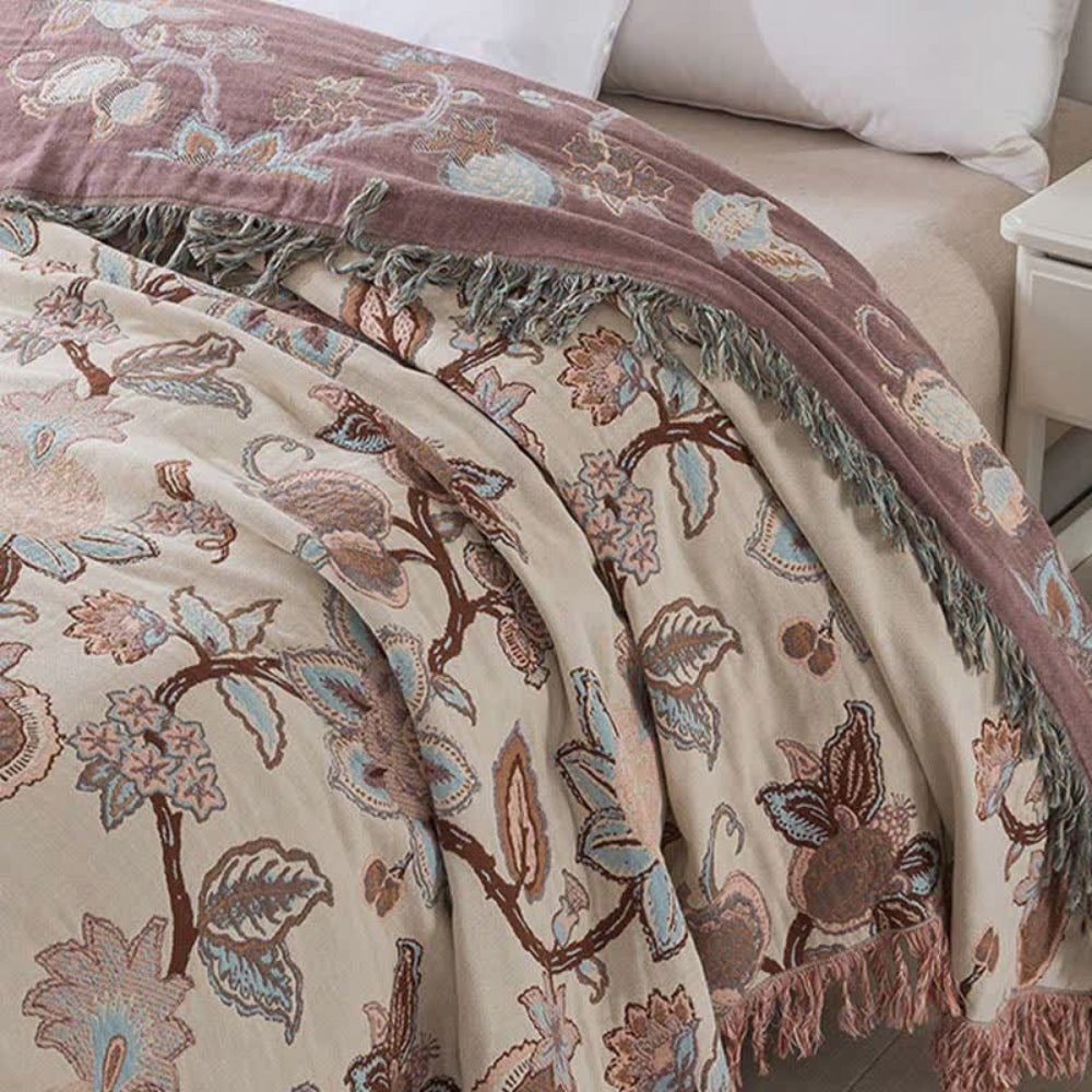 A floral cotton bed blanket with a dusty rose border and tassels.