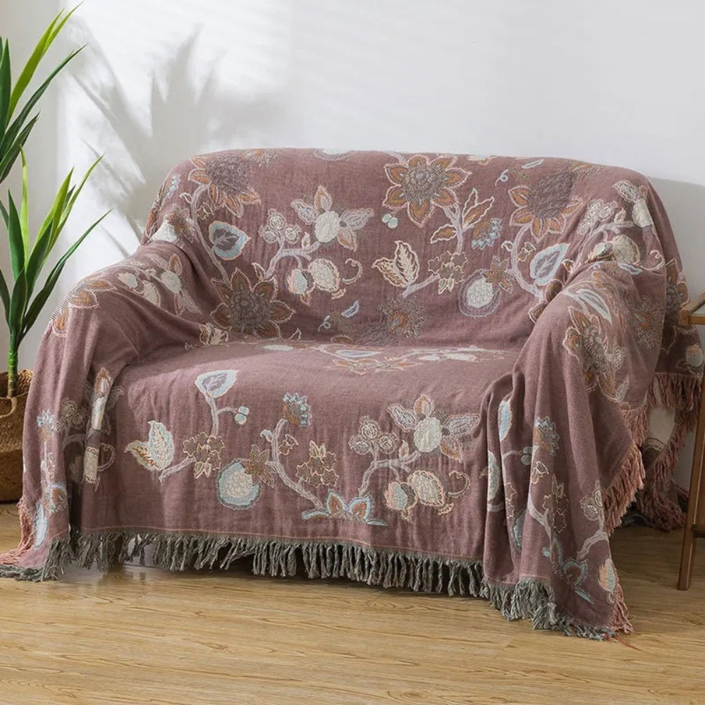 Dusty Rose Bloom Orchid Trail floral cotton blanket with tassels draped over a sofa.