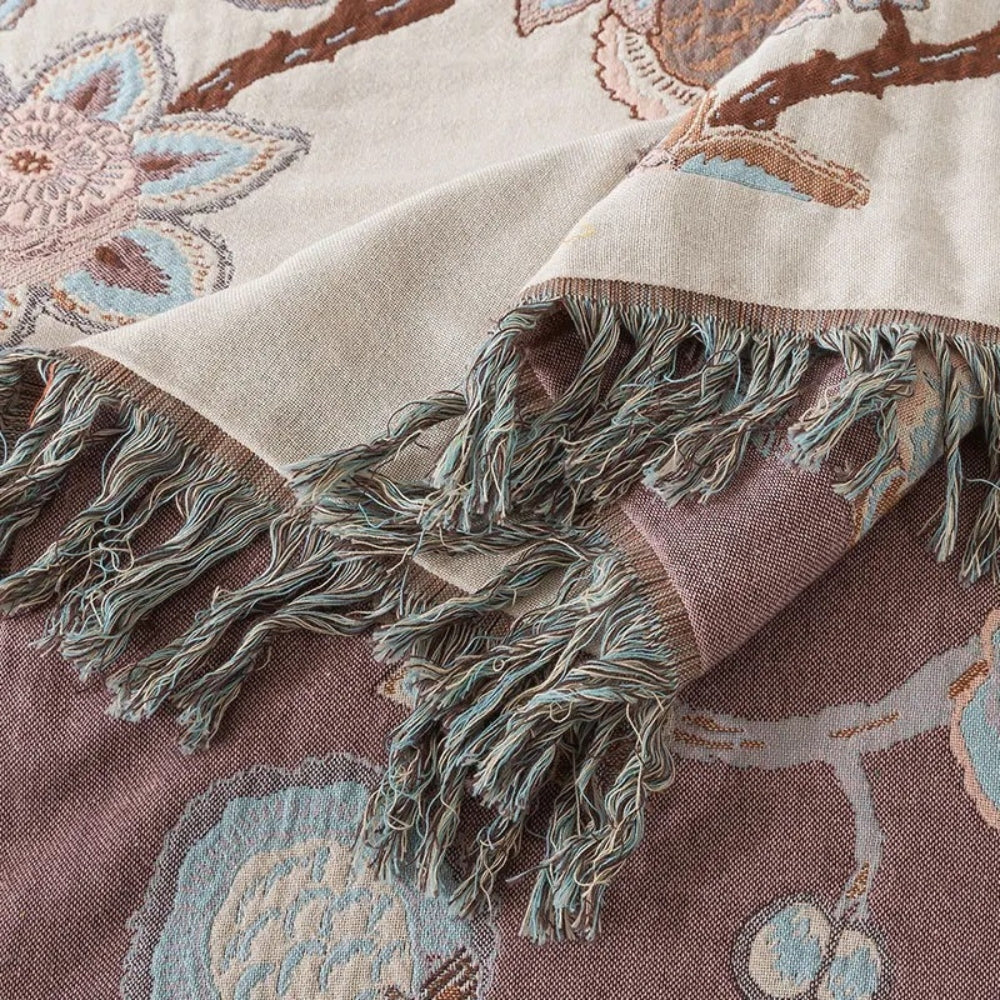Close-up of a woven cotton blanket with a floral pattern and fringed edges in shades of cream, brown, and blue.