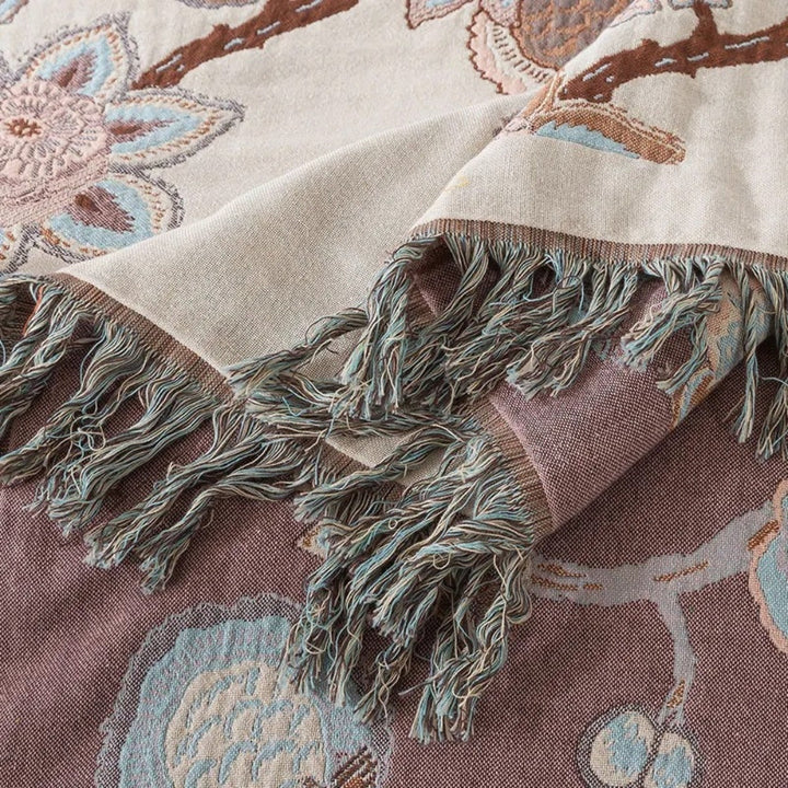 Close-up of a woven cotton blanket with a floral pattern and fringed edges in shades of cream, brown, and blue.