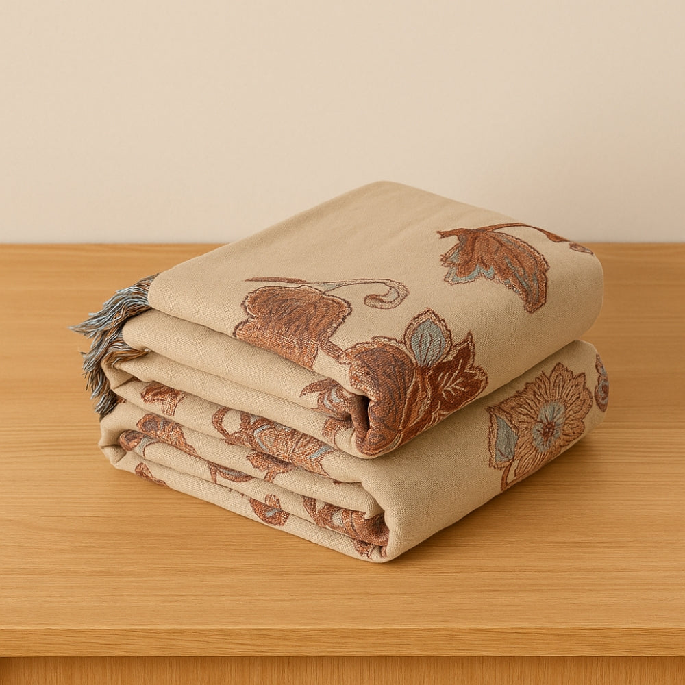 A folded beige cotton blanket with a floral pattern and blue tassels.