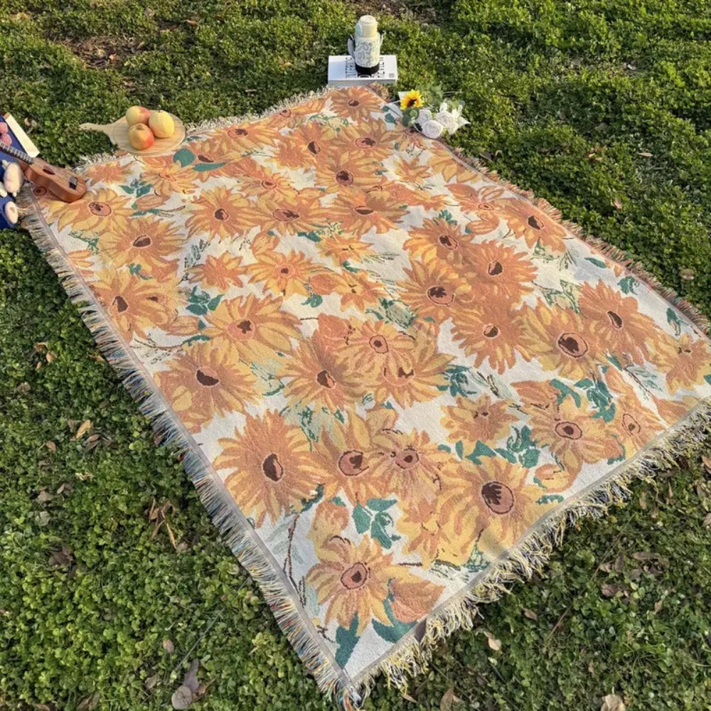 Floral picnic blanket with sunflowers laid out on green grass.