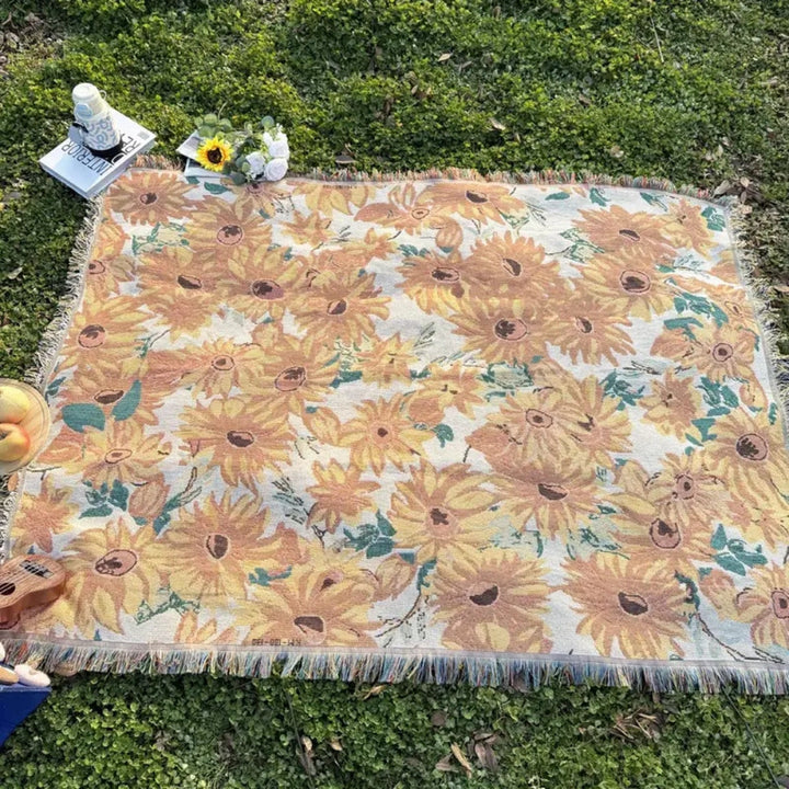 Floral picnic blanket with sunflowers laid out on grass with a book and flowers.