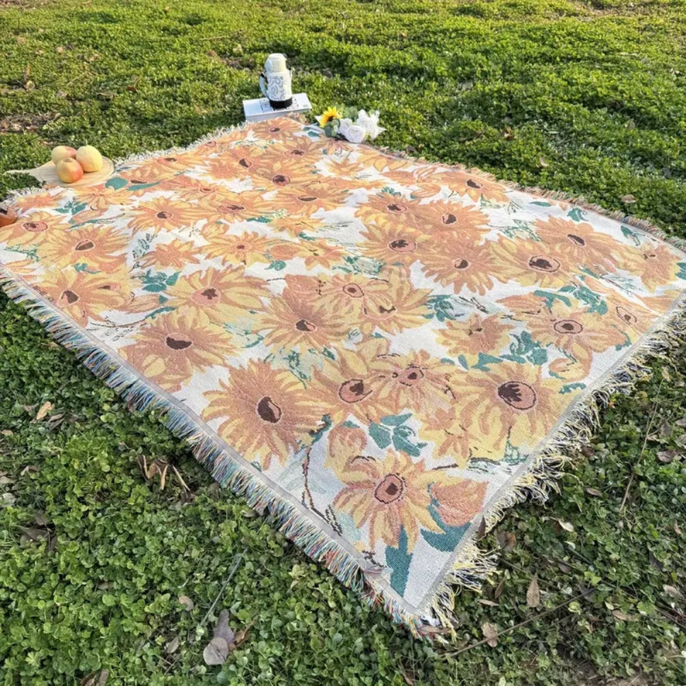 A picnic blanket with a yellow and orange floral pattern spread on green grass.