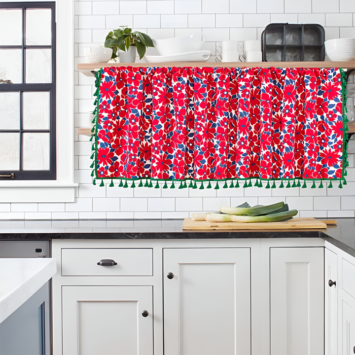 Red floral cabinet curtain with green tassels hanging in a kitchen.