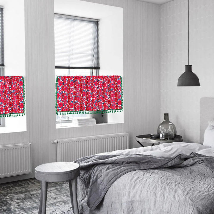 Red floral cabinet curtain with green tassels hanging in a window.