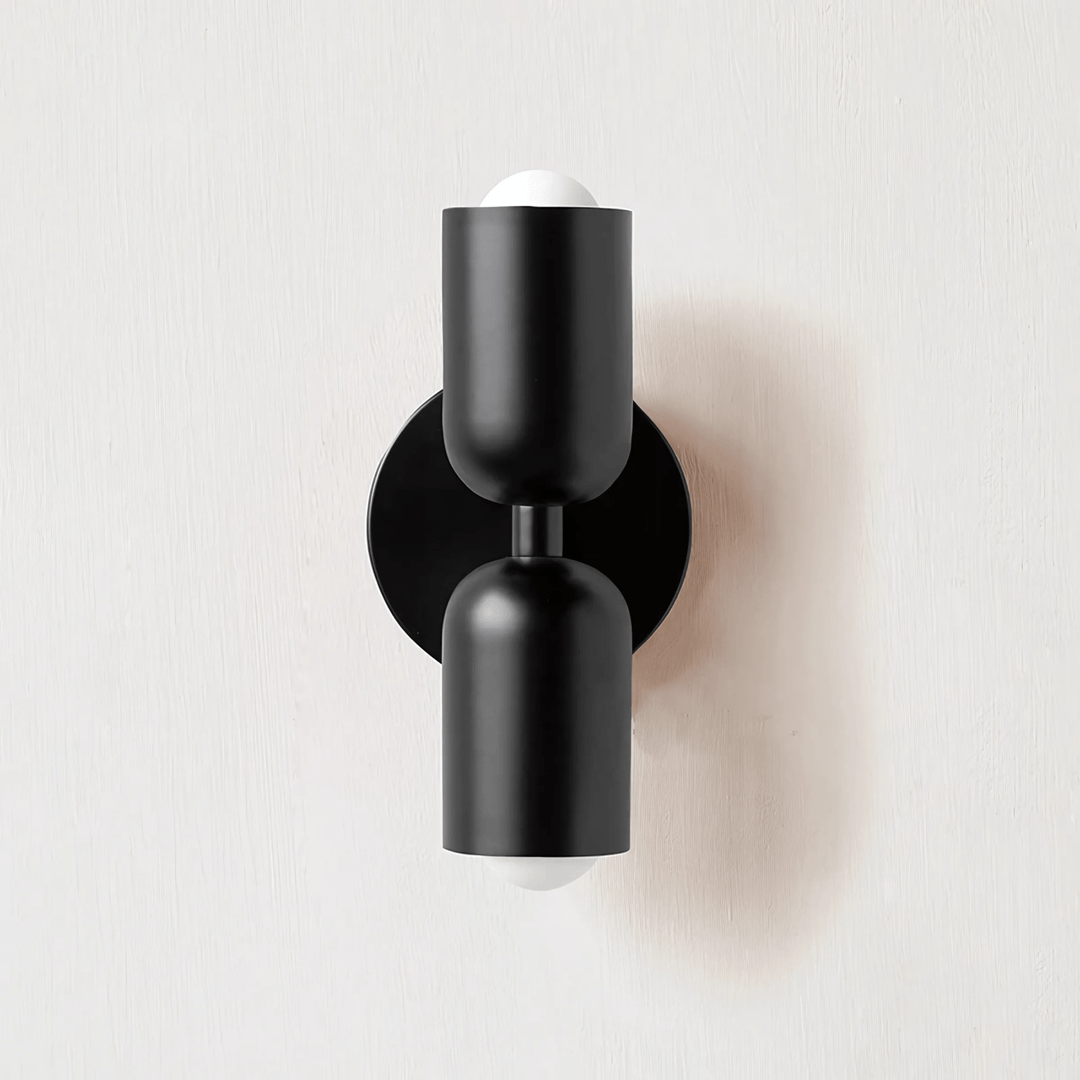 Black metal wall sconce with two cylindrical shades and exposed white bulbs.