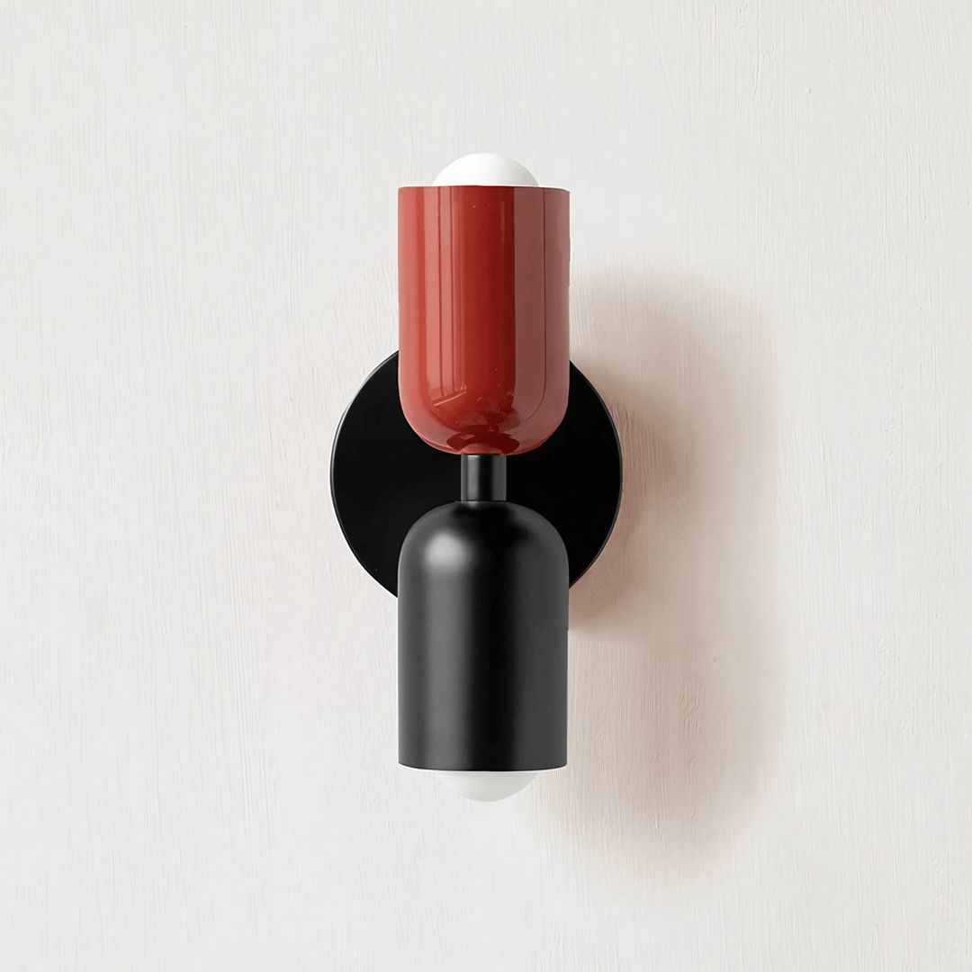 Black and red metal wall sconce with a white bulb on top and bottom, mounted on a black circular plate.