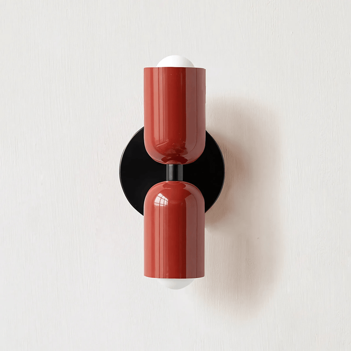 Red metal wall sconce with a black circular backplate and two white bulbs.