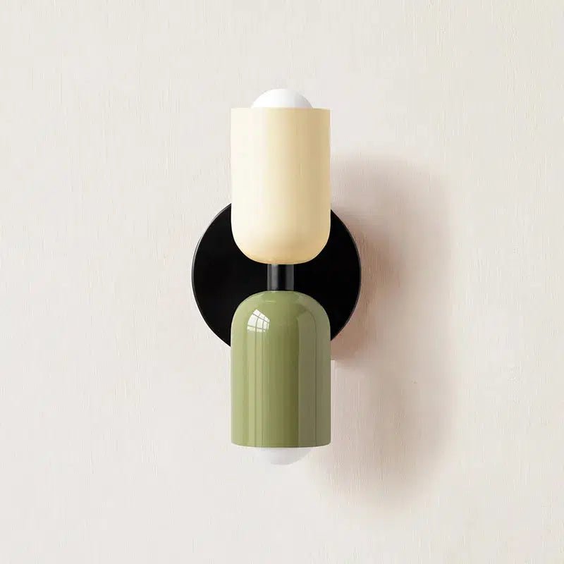 A wall sconce with a black circular base, a cream-colored cylindrical shade above a green cylindrical shade.