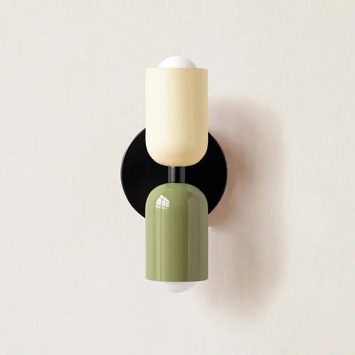 A wall sconce with a black circular base, a cream-colored cylindrical shade above a green cylindrical shade.