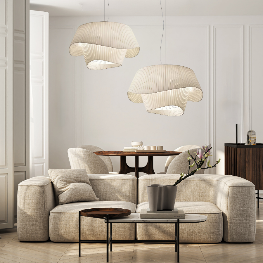 Two cream-colored pleated pendant lights hang over a beige sectional sofa in a bright living room.
